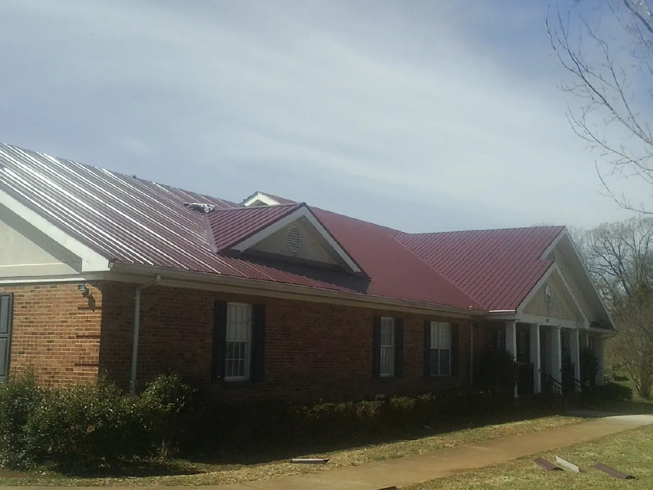 Red metal roof with gabled entries on a long brick building, from a Hail Damage Roof Repair job in Hockessin