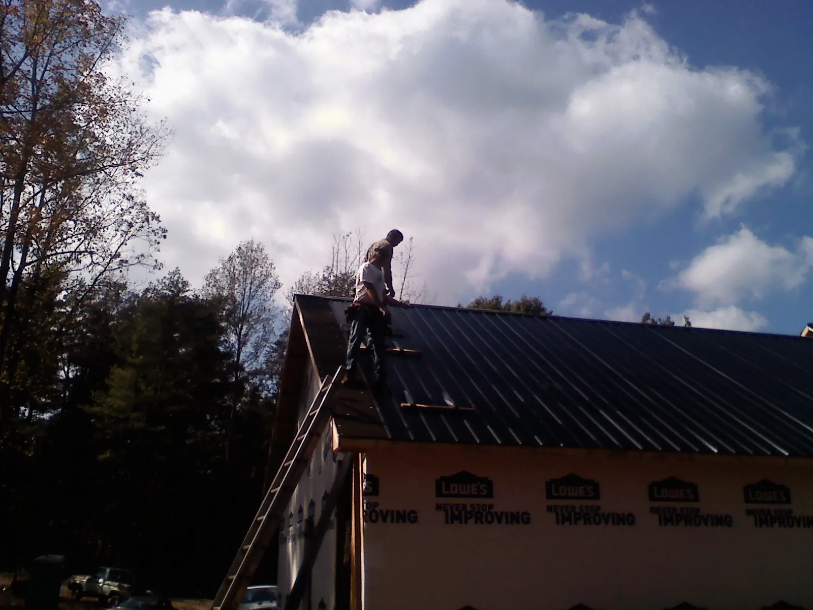 Roofer fastening dark metal panels high against a cloudy sky, from a Roof Inspection job in Hockessin