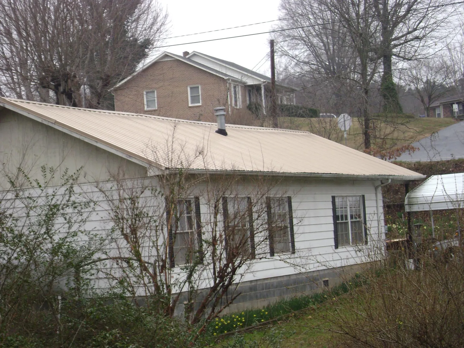 Tan metal roof on a white sided house set into a hillside — Commercial Roofing by Roofing Brothers in Hockessin